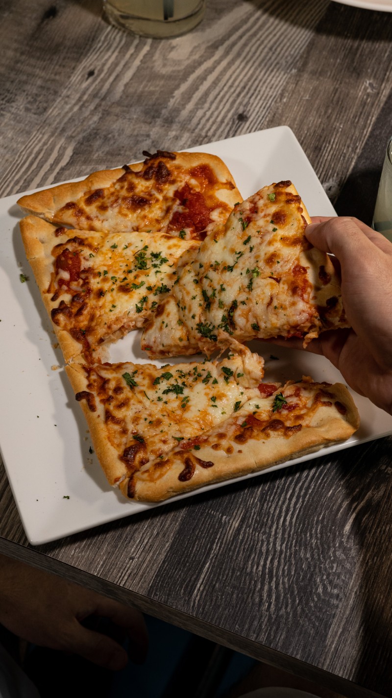 A person is grabbing a slice of pizza from a plate.