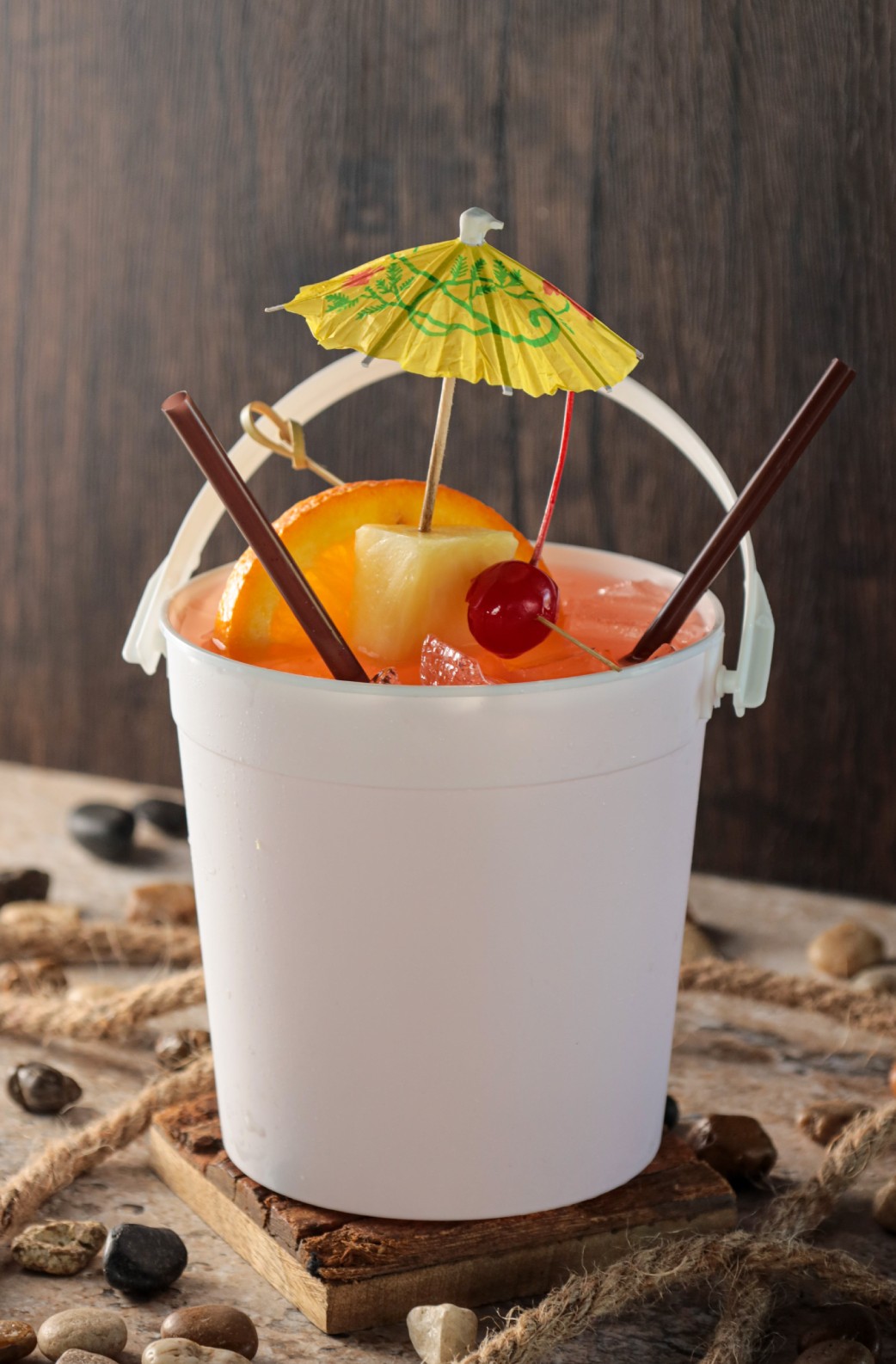 A white bucket with a drink in it and an umbrella.