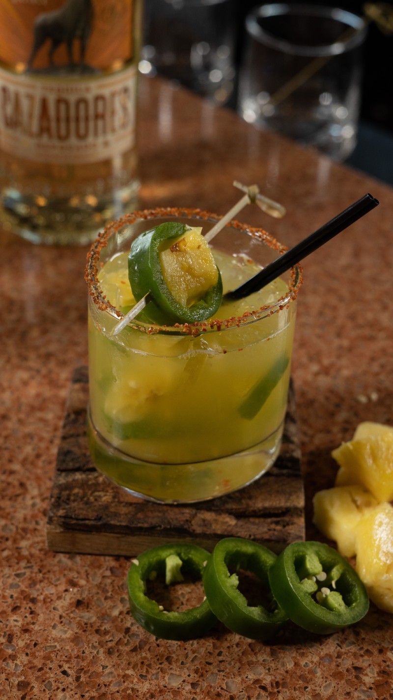 A cocktail with jalapeno peppers and a straw.