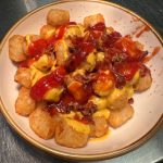 A bowl of tater tots with ketchup and bacon.
