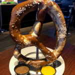 A pretzel on a plate with dips on it.